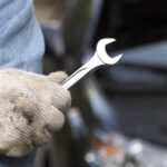 man-holding-wrench-with-car-in-background
