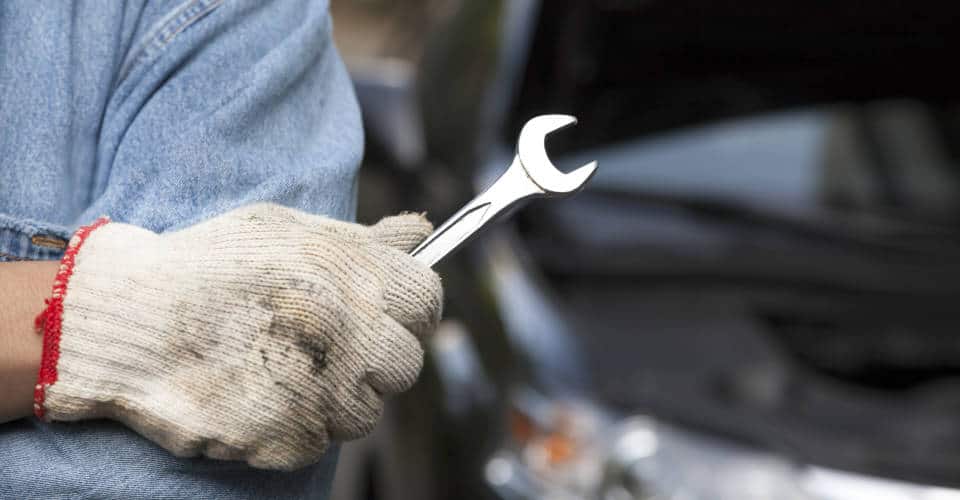 man holding wrench with car in background 1